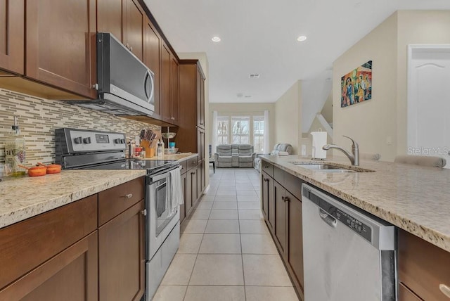 kitchen featuring sink, light tile patterned floors, stainless steel appliances, light stone counters, and decorative backsplash