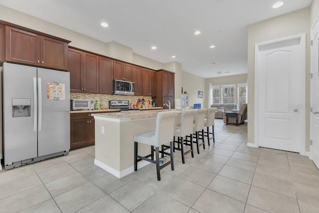 kitchen featuring a breakfast bar area, a center island with sink, appliances with stainless steel finishes, light stone countertops, and backsplash