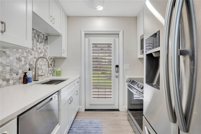 kitchen with appliances with stainless steel finishes, white cabinetry, sink, backsplash, and light wood-type flooring