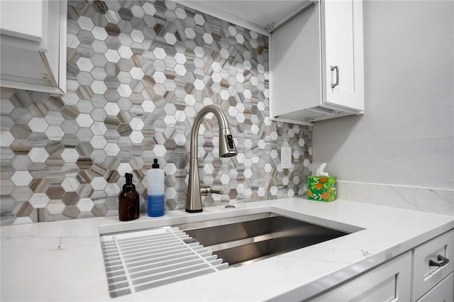 kitchen with sink, light stone counters, white cabinets, and backsplash