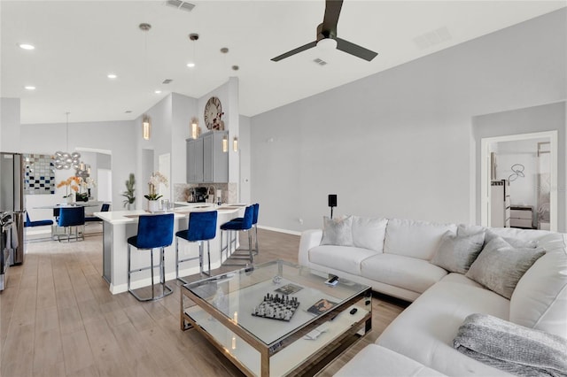 living room with ceiling fan with notable chandelier, vaulted ceiling, and light wood-type flooring