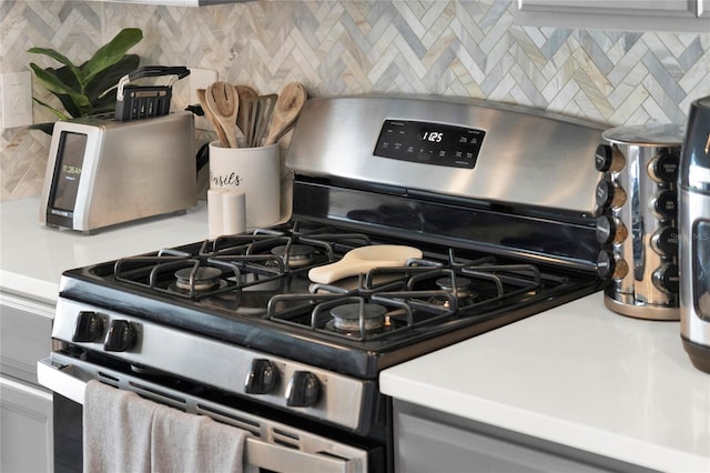 details with gray cabinets, stainless steel range with gas cooktop, and decorative backsplash