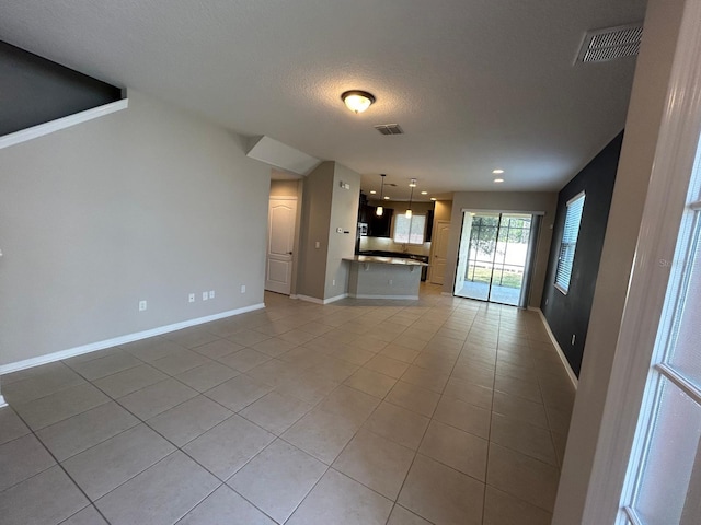 unfurnished living room with light tile patterned floors, baseboards, visible vents, and a textured ceiling