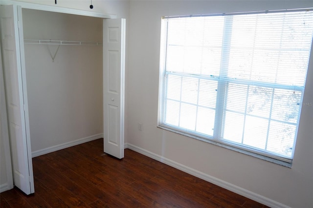 unfurnished bedroom with a closet, dark hardwood / wood-style flooring, and multiple windows