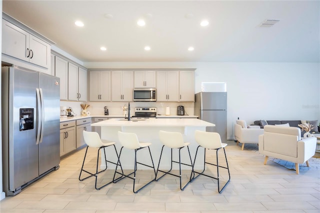 kitchen featuring stainless steel appliances, a breakfast bar, a kitchen island with sink, and gray cabinetry