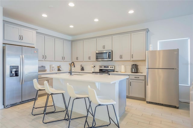 kitchen featuring sink, a kitchen breakfast bar, stainless steel appliances, a kitchen island with sink, and decorative backsplash