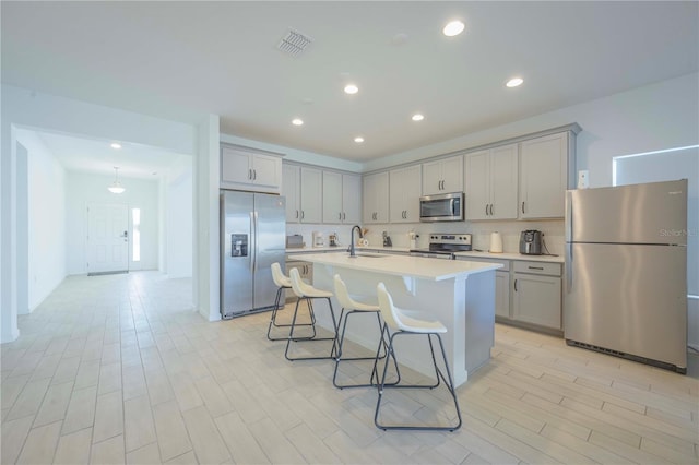 kitchen with appliances with stainless steel finishes, tasteful backsplash, an island with sink, sink, and a kitchen breakfast bar