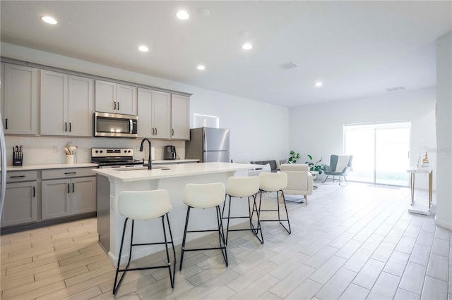 kitchen featuring tasteful backsplash, a breakfast bar area, gray cabinetry, a kitchen island with sink, and stainless steel appliances