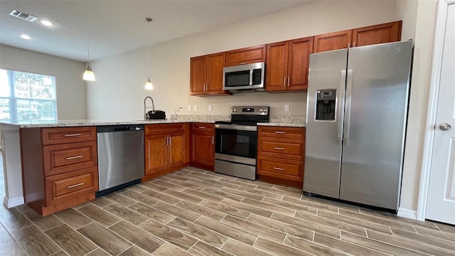 kitchen with light stone counters, appliances with stainless steel finishes, sink, and hanging light fixtures