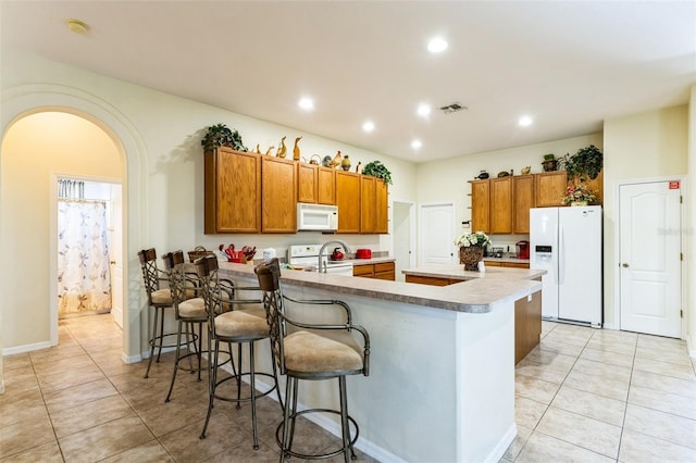 kitchen with white appliances, a kitchen island with sink, a breakfast bar area, and light tile patterned floors