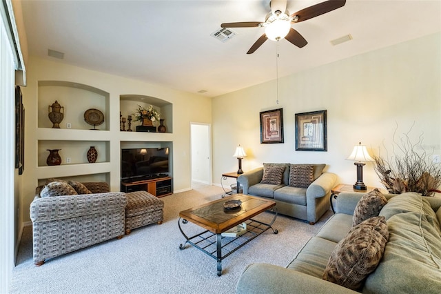 living area with built in features, light colored carpet, visible vents, and ceiling fan