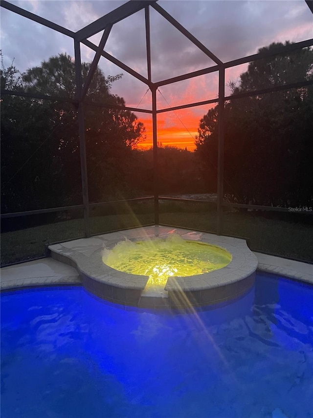 pool at dusk with an in ground hot tub, glass enclosure, and an outdoor pool