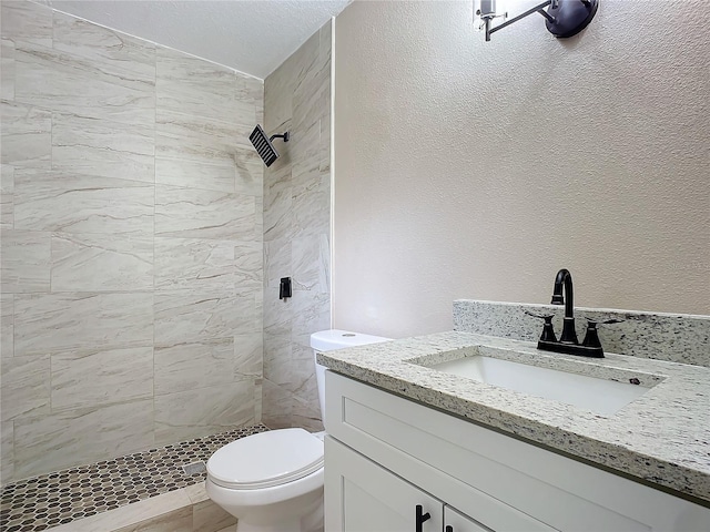 bathroom with vanity, tiled shower, and toilet