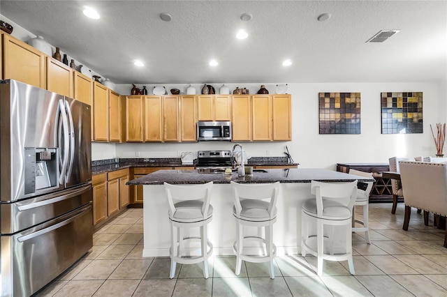 kitchen with light tile patterned floors, a breakfast bar area, stainless steel appliances, and an island with sink