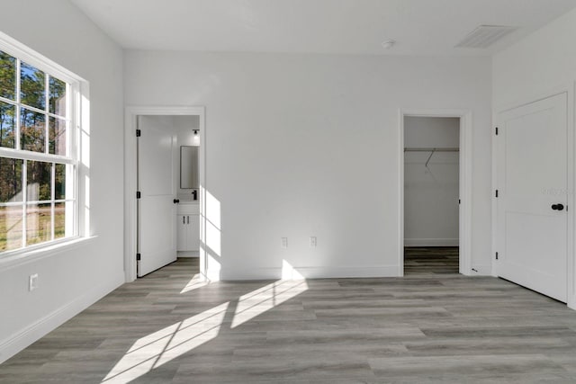 unfurnished bedroom with multiple windows, a walk in closet, a closet, and light wood-type flooring