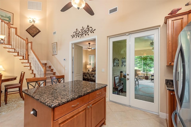 kitchen with light tile patterned floors, stainless steel fridge, ceiling fan, a kitchen island, and dark stone counters