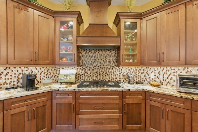 kitchen featuring tasteful backsplash, custom range hood, stainless steel gas cooktop, and light stone counters