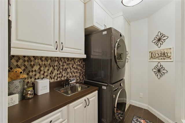 clothes washing area with stacked washer and dryer, sink, cabinets, and dark tile patterned floors