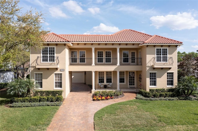 mediterranean / spanish home featuring a tile roof, a front yard, stucco siding, and a balcony