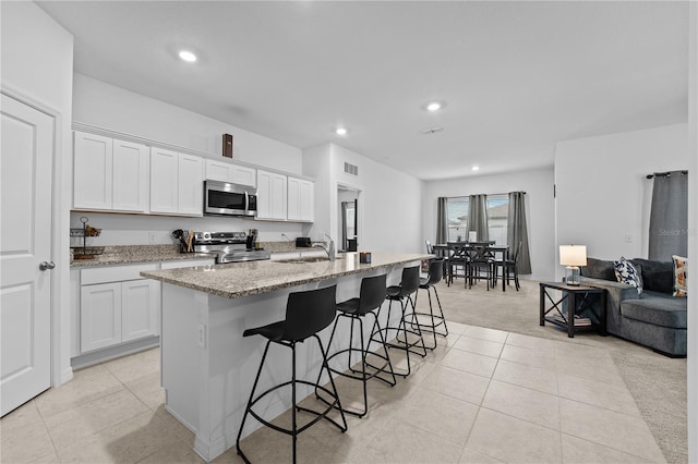 kitchen with a breakfast bar area, a kitchen island with sink, stainless steel appliances, light stone counters, and white cabinets