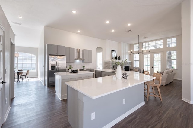 kitchen featuring gray cabinets, a kitchen island, appliances with stainless steel finishes, pendant lighting, and wall chimney range hood