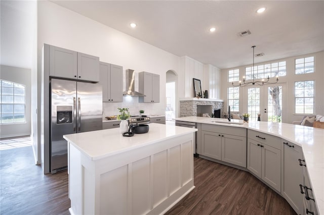 kitchen featuring sink, stainless steel fridge, gray cabinets, decorative light fixtures, and wall chimney exhaust hood