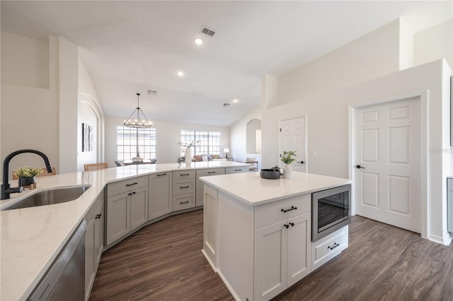 kitchen featuring built in microwave, lofted ceiling, sink, decorative light fixtures, and dishwasher