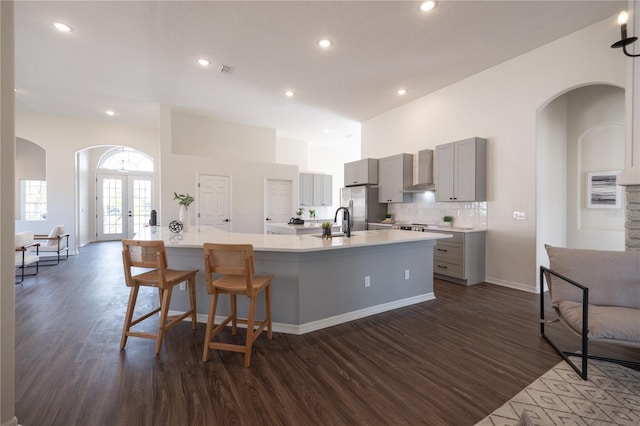 kitchen featuring stainless steel fridge with ice dispenser, dark hardwood / wood-style floors, gray cabinets, a large island, and wall chimney range hood