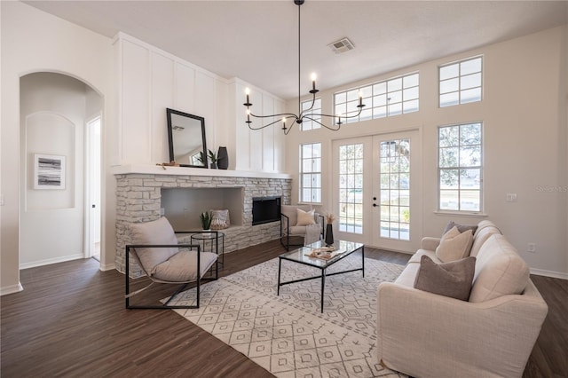 living room with a stone fireplace, hardwood / wood-style floors, a notable chandelier, and french doors