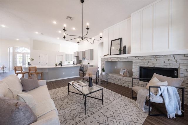 living room with a notable chandelier, sink, a stone fireplace, and hardwood / wood-style floors