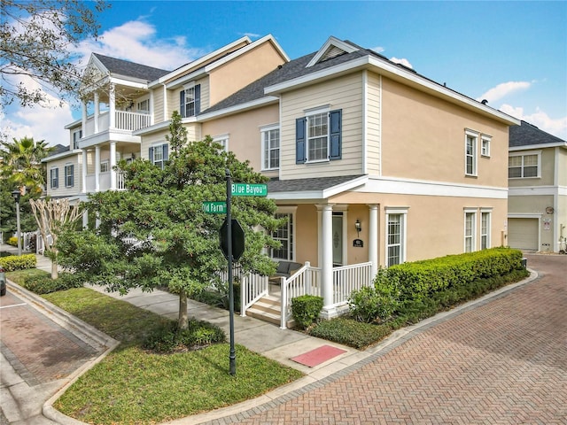 townhome / multi-family property featuring covered porch, stucco siding, and a shingled roof