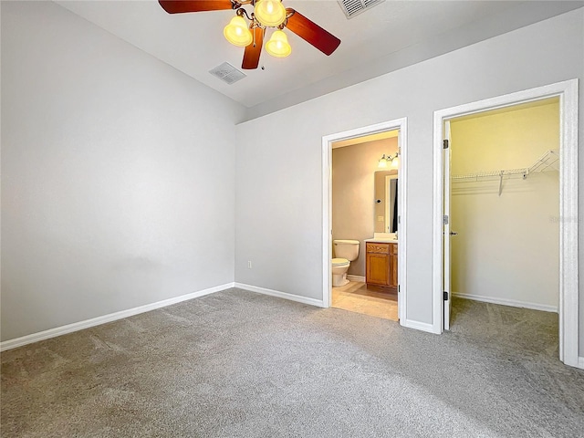 unfurnished bedroom with baseboards, visible vents, ensuite bath, light carpet, and a walk in closet