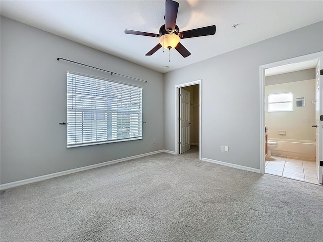 unfurnished bedroom featuring a walk in closet, multiple windows, light colored carpet, and baseboards