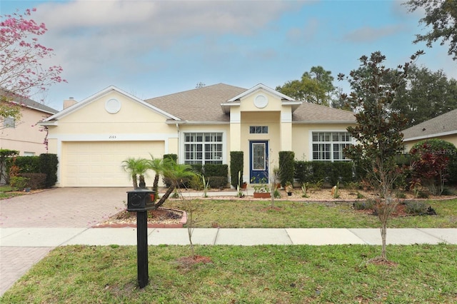 single story home with an attached garage, a front yard, decorative driveway, and stucco siding