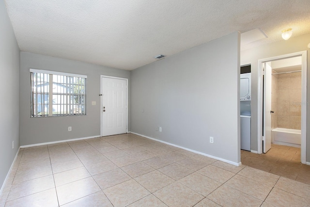 tiled spare room featuring stacked washer / dryer and a textured ceiling