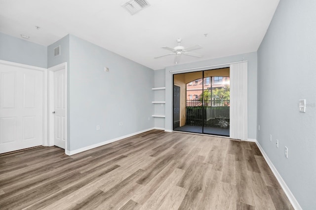 spare room with built in shelves, ceiling fan, and light hardwood / wood-style floors