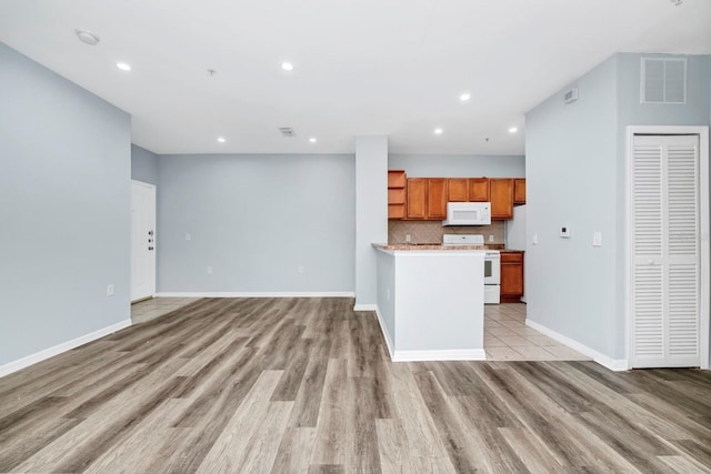 kitchen with tasteful backsplash, white appliances, and light hardwood / wood-style flooring