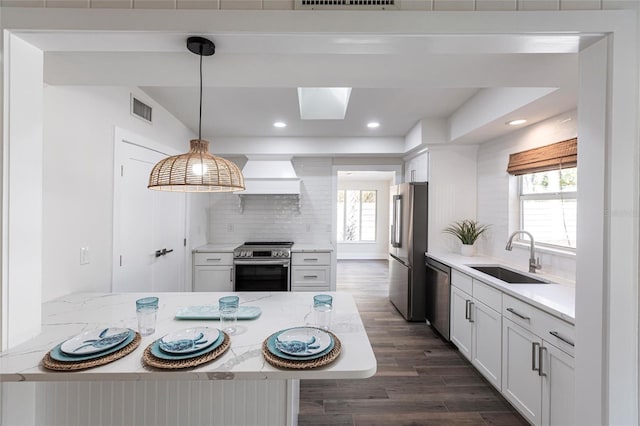 kitchen with sink, appliances with stainless steel finishes, white cabinetry, hanging light fixtures, and light stone counters