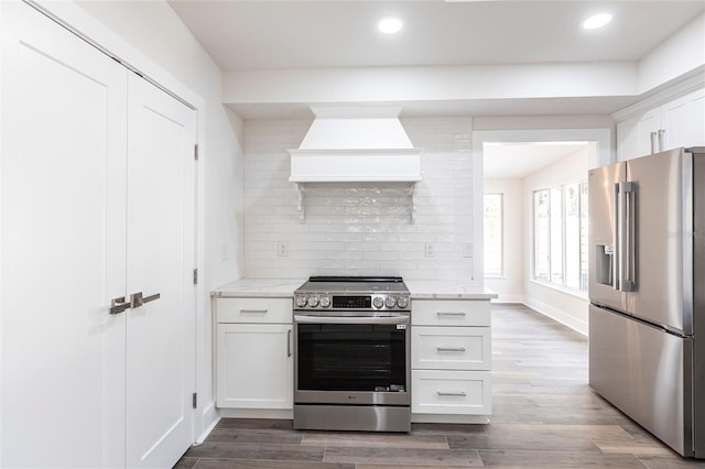 kitchen featuring tasteful backsplash, white cabinetry, stainless steel appliances, light stone countertops, and custom range hood