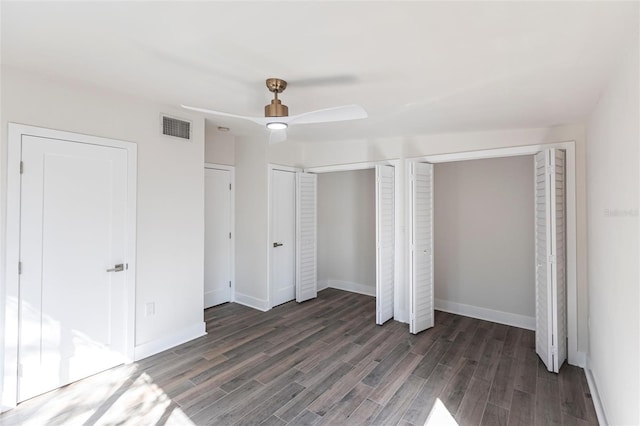 unfurnished bedroom with ceiling fan, two closets, and dark hardwood / wood-style flooring