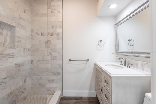 bathroom with vanity, wood-type flooring, a tile shower, and toilet