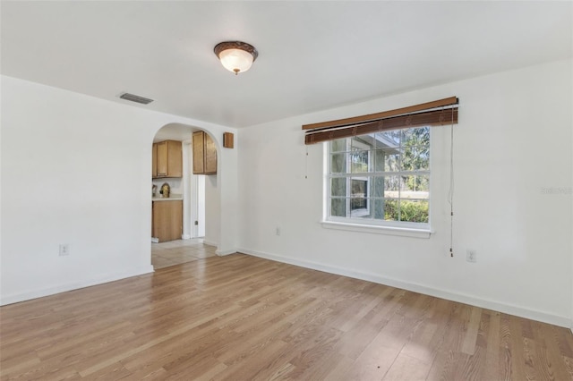 unfurnished room with arched walkways, baseboards, visible vents, and light wood finished floors