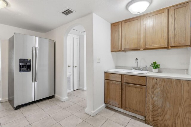 kitchen featuring stainless steel fridge, visible vents, arched walkways, a sink, and light tile patterned flooring