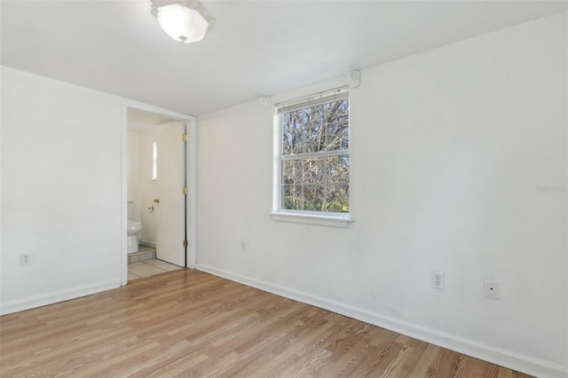 unfurnished bedroom featuring light wood-style floors, baseboards, and connected bathroom