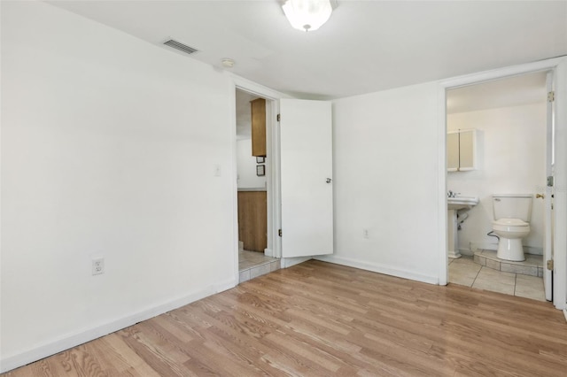 unfurnished bedroom with baseboards, connected bathroom, visible vents, and wood finished floors