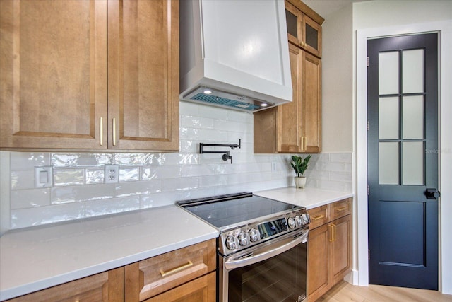 kitchen with wall chimney range hood, decorative backsplash, light hardwood / wood-style flooring, and stainless steel range with electric cooktop