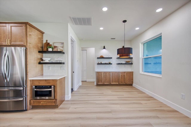 kitchen featuring stainless steel appliances, pendant lighting, backsplash, and light hardwood / wood-style flooring