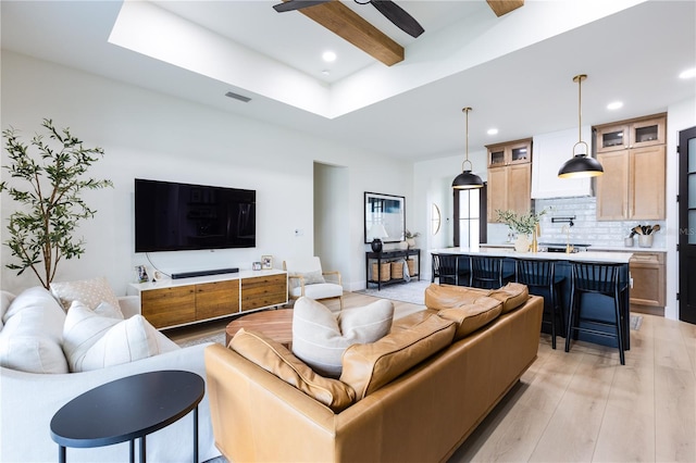 living room with beam ceiling, a skylight, ceiling fan, and light hardwood / wood-style flooring