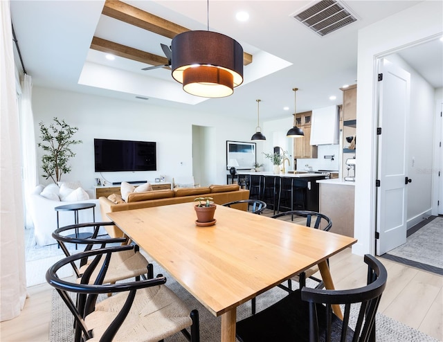 dining space with a raised ceiling, ceiling fan, and light hardwood / wood-style floors