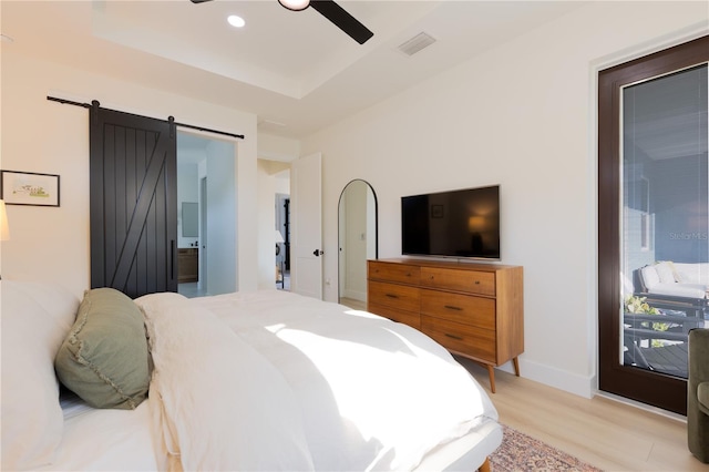 bedroom with ceiling fan, a barn door, a raised ceiling, and light hardwood / wood-style floors